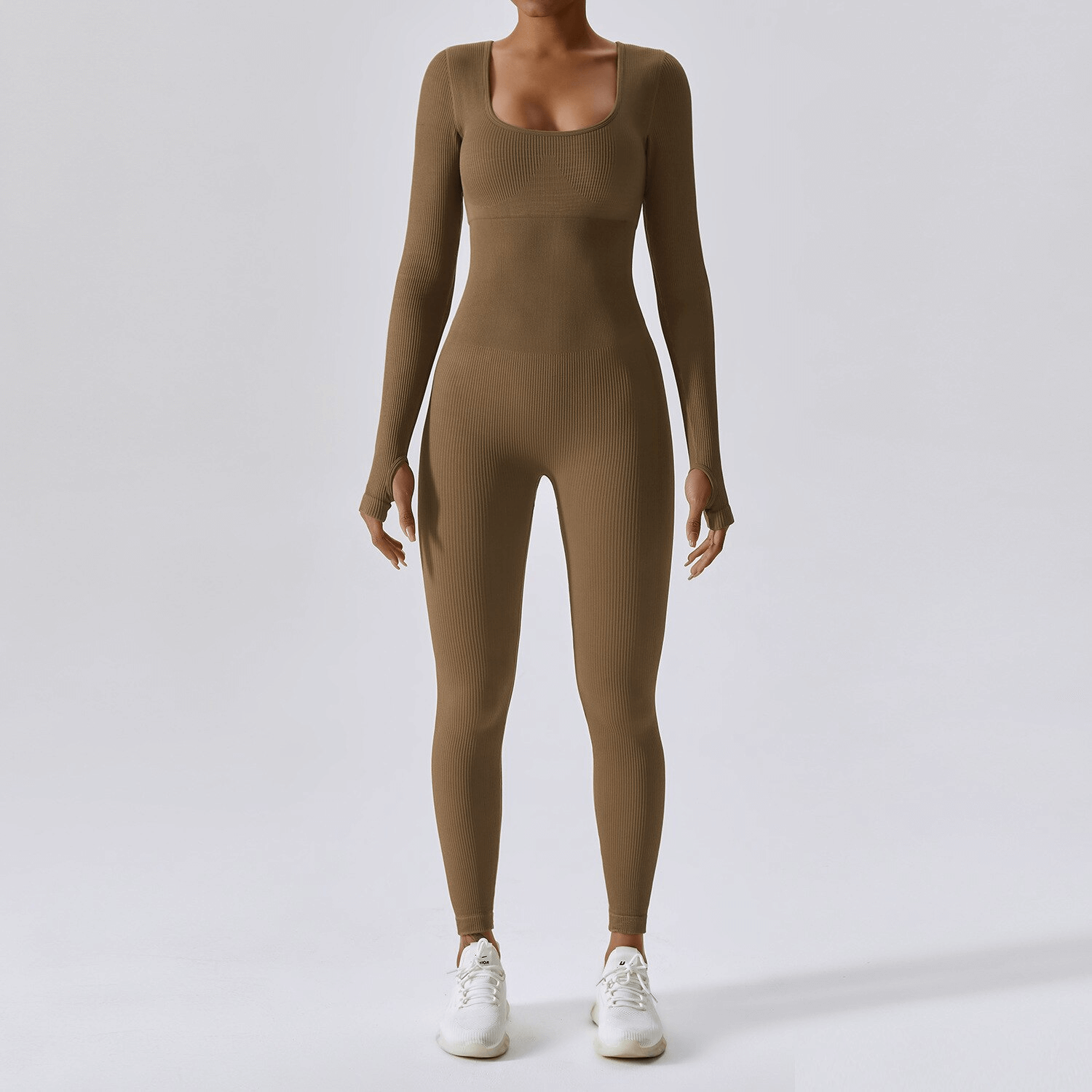 Seamless brown yoga suit with thumb holes for women, designed for fitness and athleisure. Model wearing full-length jumpsuit and white sneakers.